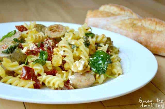 white dinner plate with sundried tomato pasta and a loaf of French bread next to it