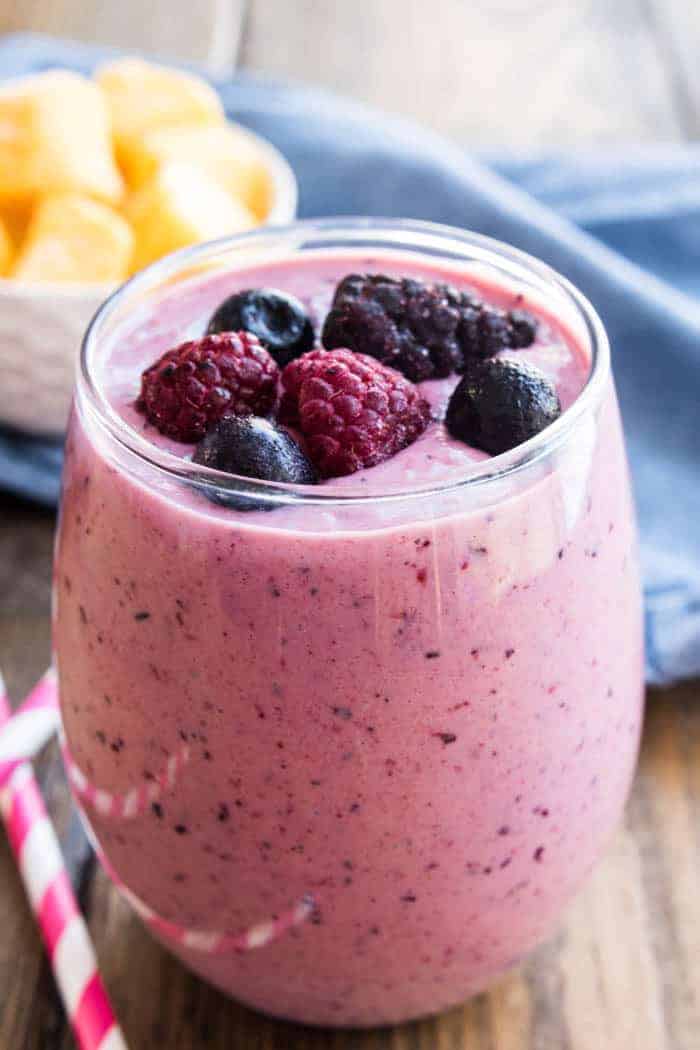 A glass with a Mango-Berry fruit Smoothie and fresh berries in it