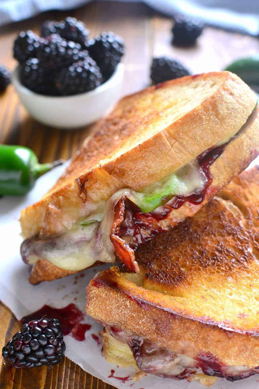 Blackberry Bacon Grilled Cheese cut in half next to a bowl of fresh blackberries