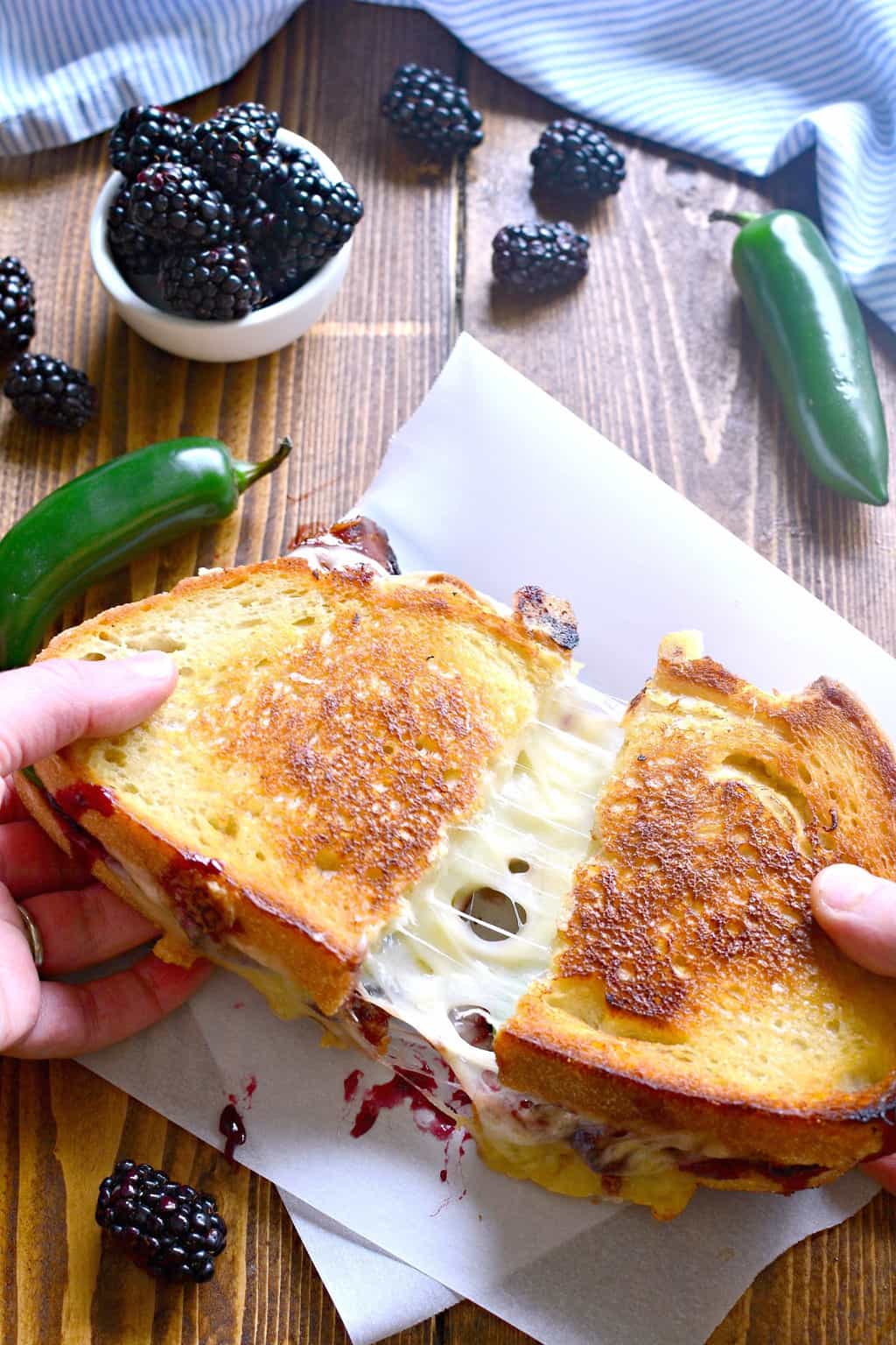 hands pulling apart a Blackberry Bacon Grilled Cheese so you can see the melted cheese stretching between the two halves