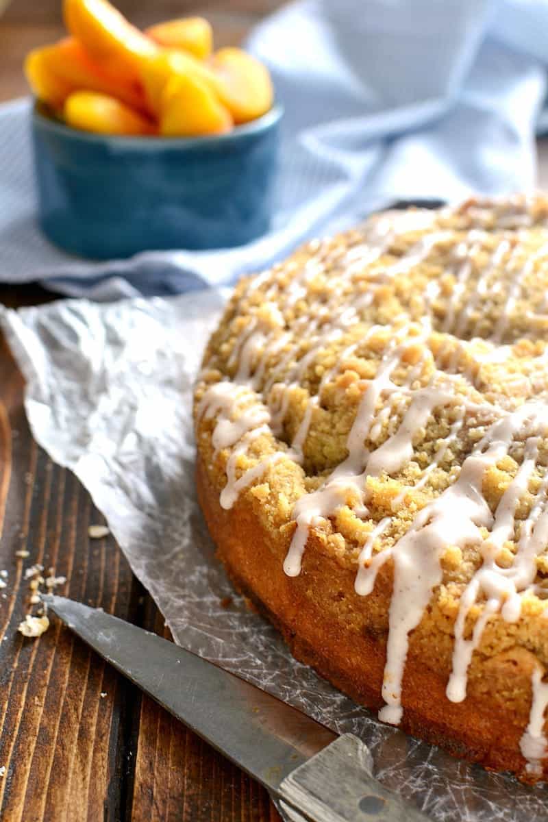 Peach Cobbler Coffee Cake sits next to a bowl of fresh peaches and a knife for slicing