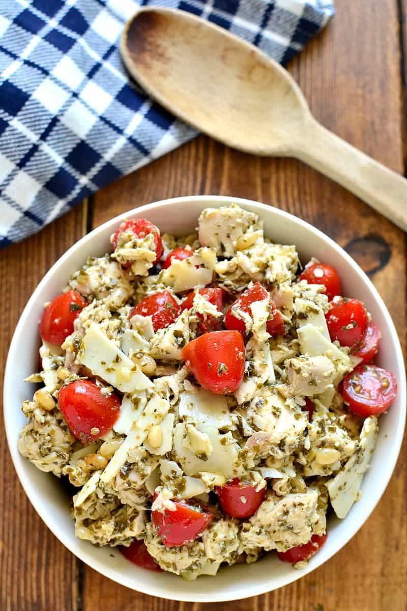 a bowl of pesto chicken salad and a wooden spoon next to it, for serving