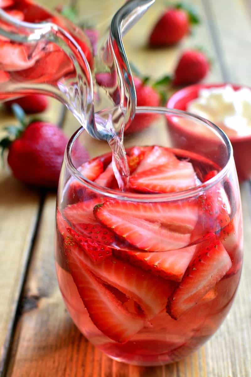 Moscato wine being poured into a glass with fresh strawberry slices to make a Strawberry Shortcake Sangria cocktail