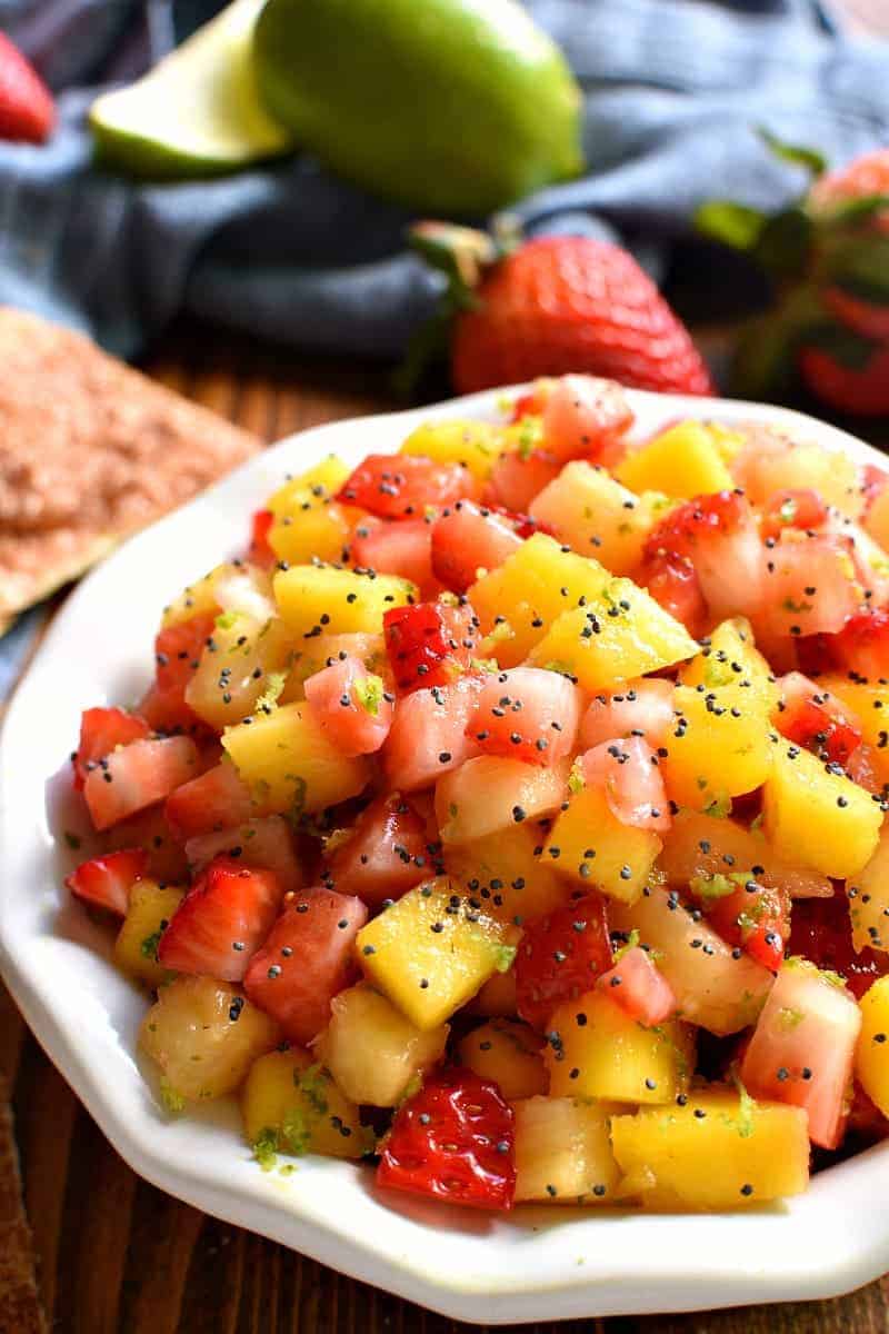 overhead image of a white bowl filled with fresh fruit salsa garnished with poppy seeds