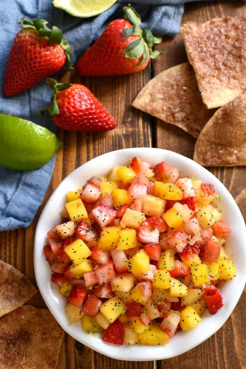 overhead image of a bowl of fruit salsa surrounded by tortilla chips and fresh strawberries