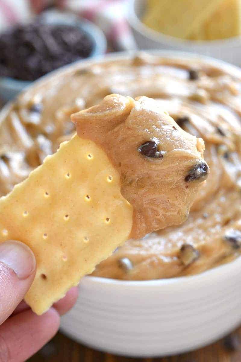 butter cracker dipped into creamy peanut butter chocolate chip dip. Bowl of the dip is behind it.