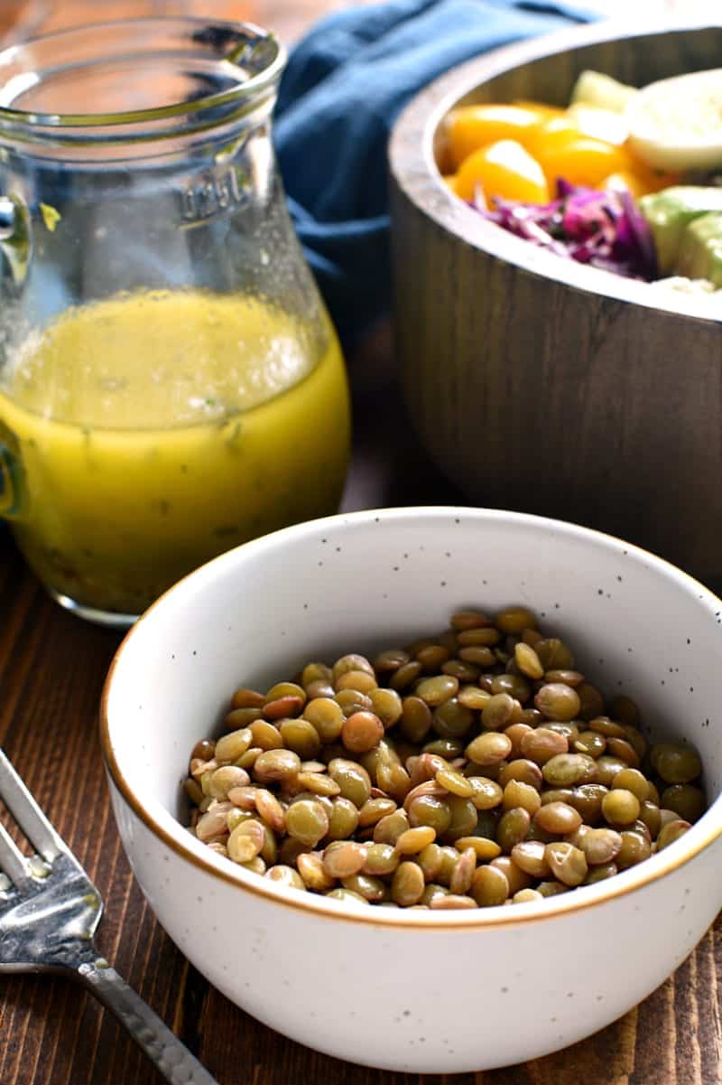 bowl of cooked lentils next to a protein power salad and cruet of salad dressing