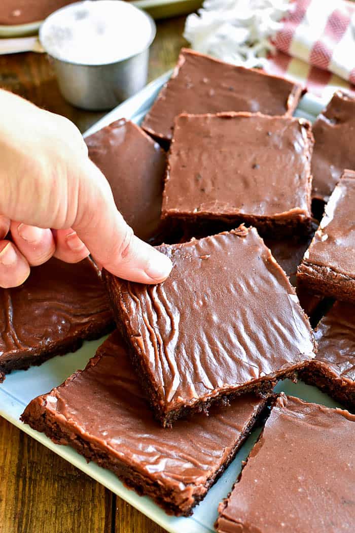 Hand grabbing frosted brownie from plate