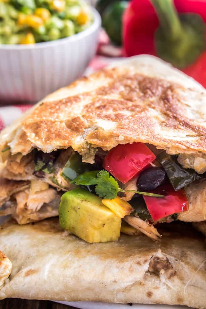 These Loaded Chicken Quesadillas have it all! Crisp tortillas stuffed with seasoned shredded chicken, bell peppers, onions, black beans, avocado, cilantro, corn, and white cheddar cheese. 