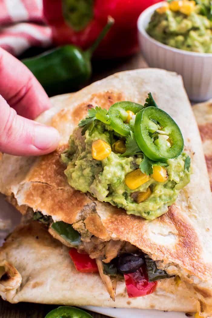These Loaded Chicken Quesadillas have it all! Crisp tortillas stuffed with seasoned shredded chicken, bell peppers, onions, black beans, avocado, cilantro, corn, and white cheddar cheese. 
