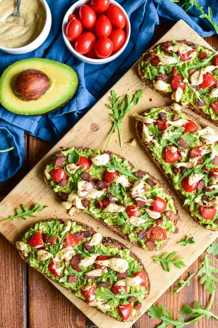 BLT Avocado Toast on wooden cutting board with ingredients in the background