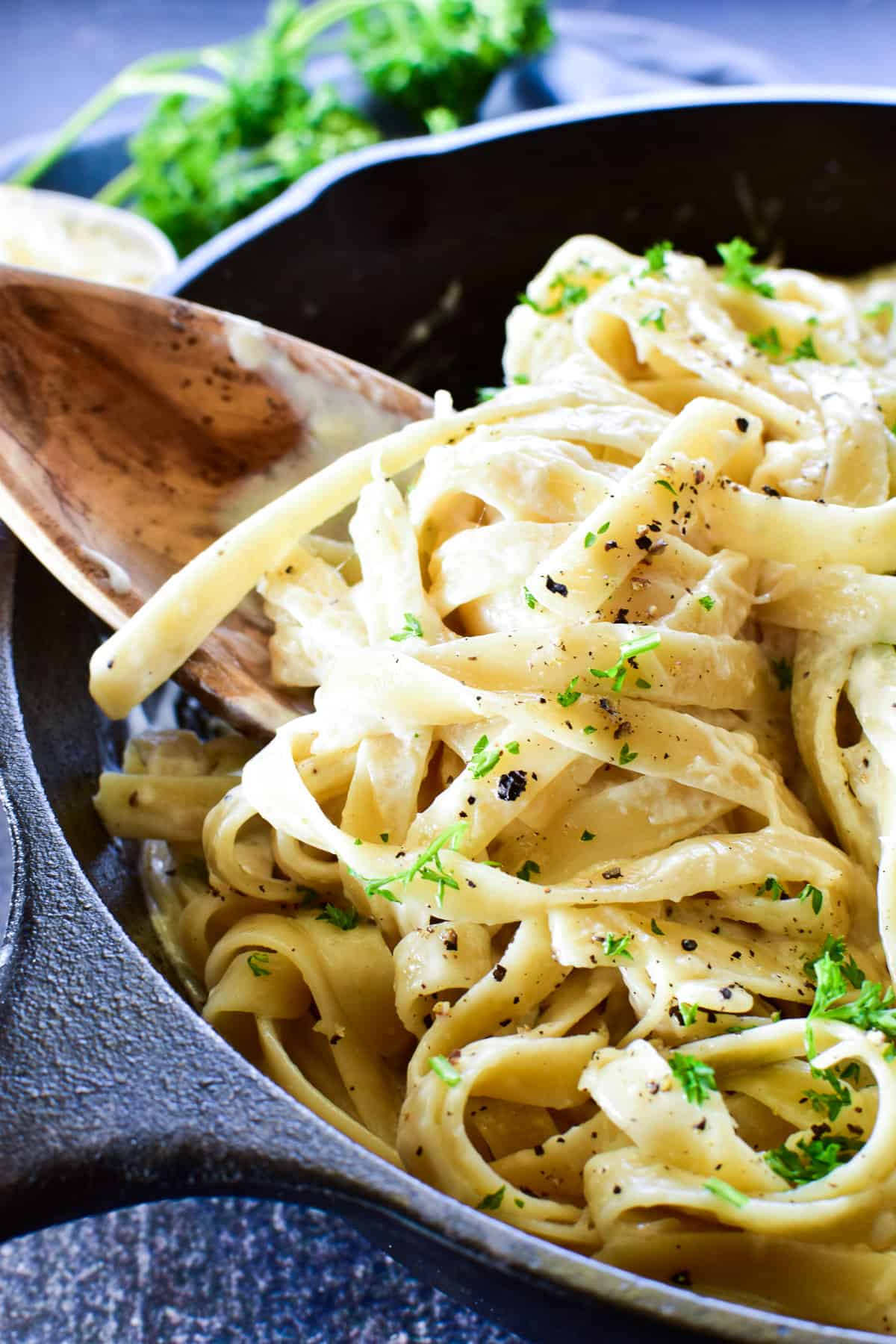 Close up of Fettuccine Alfredo in skillet with wooden serving spoon