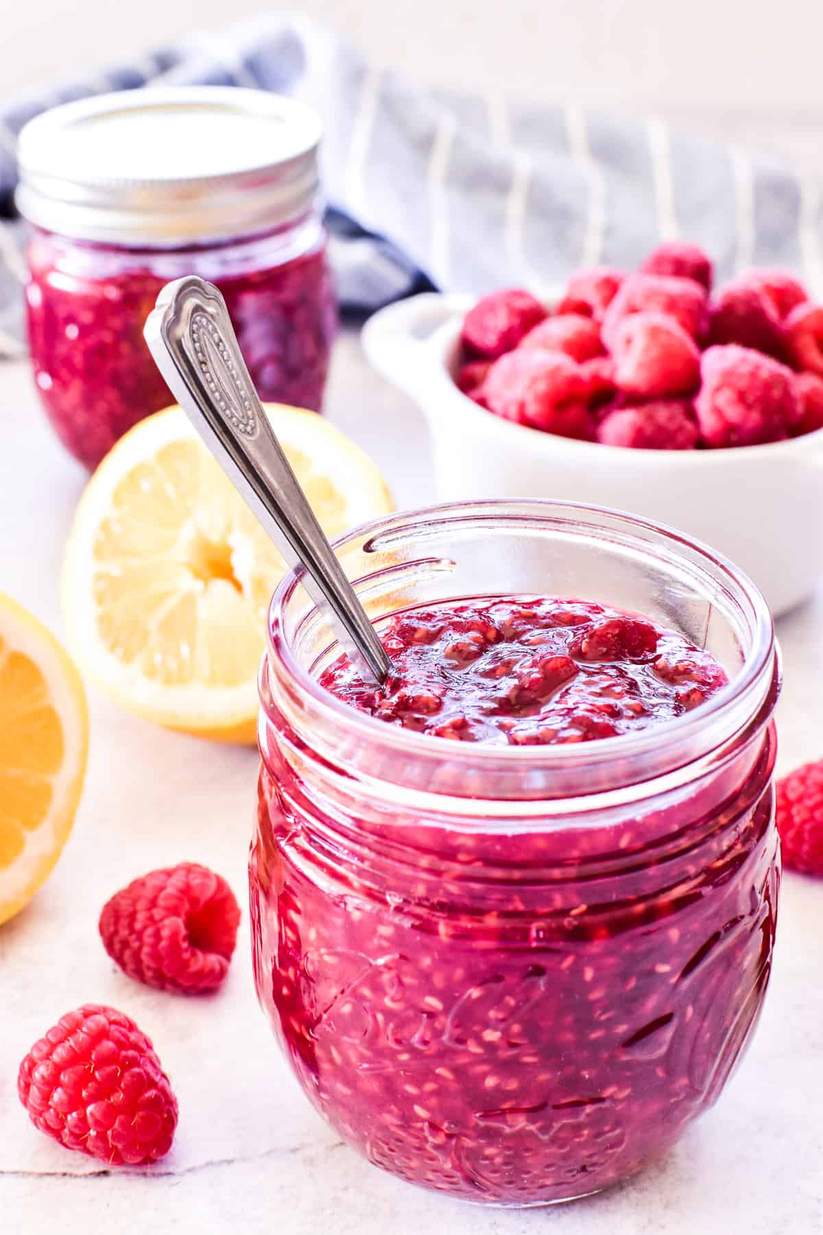 Raspberry Jam in jar with spoon and fresh ingredients in background