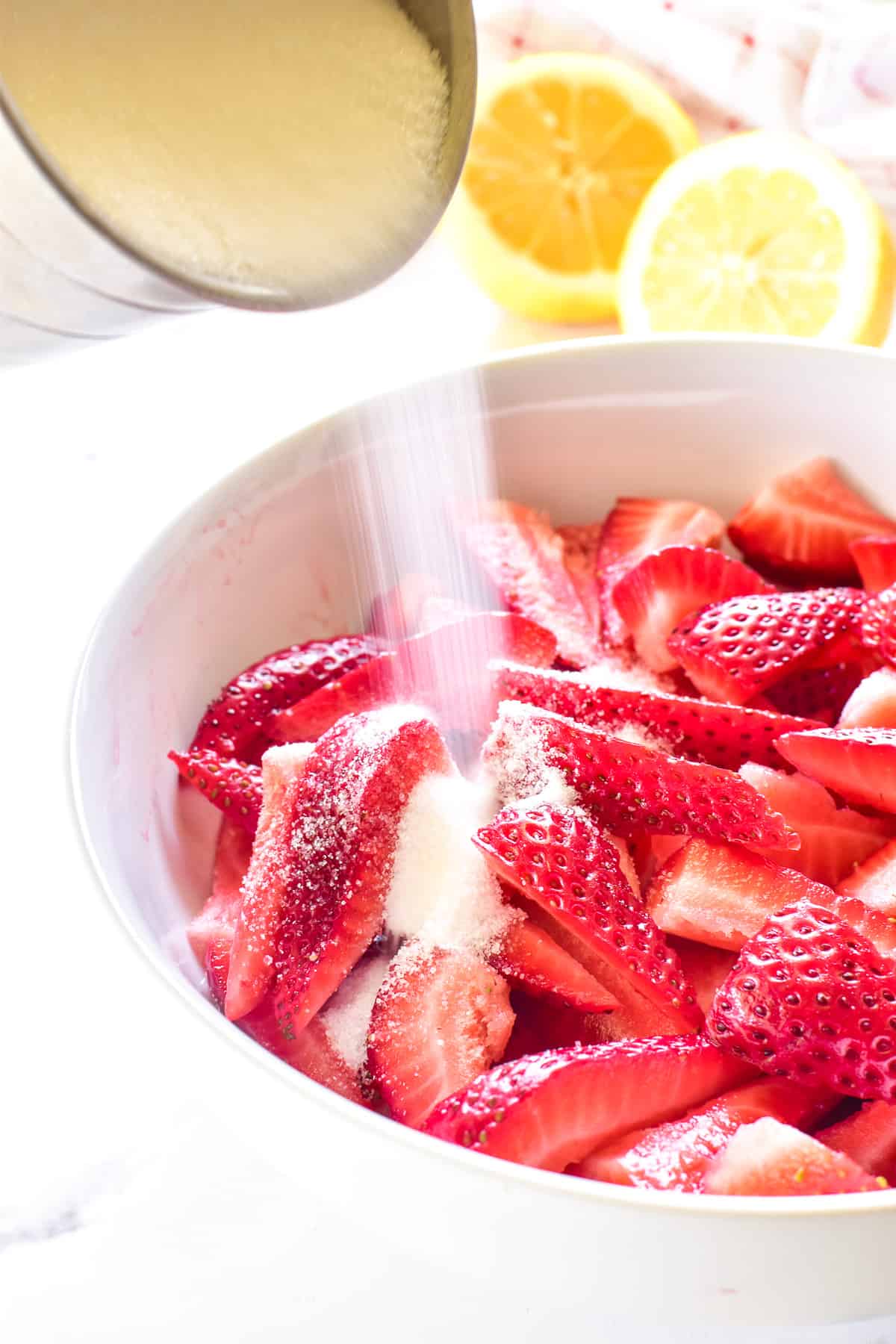 Strawberries in bowl with sugar being poured over them