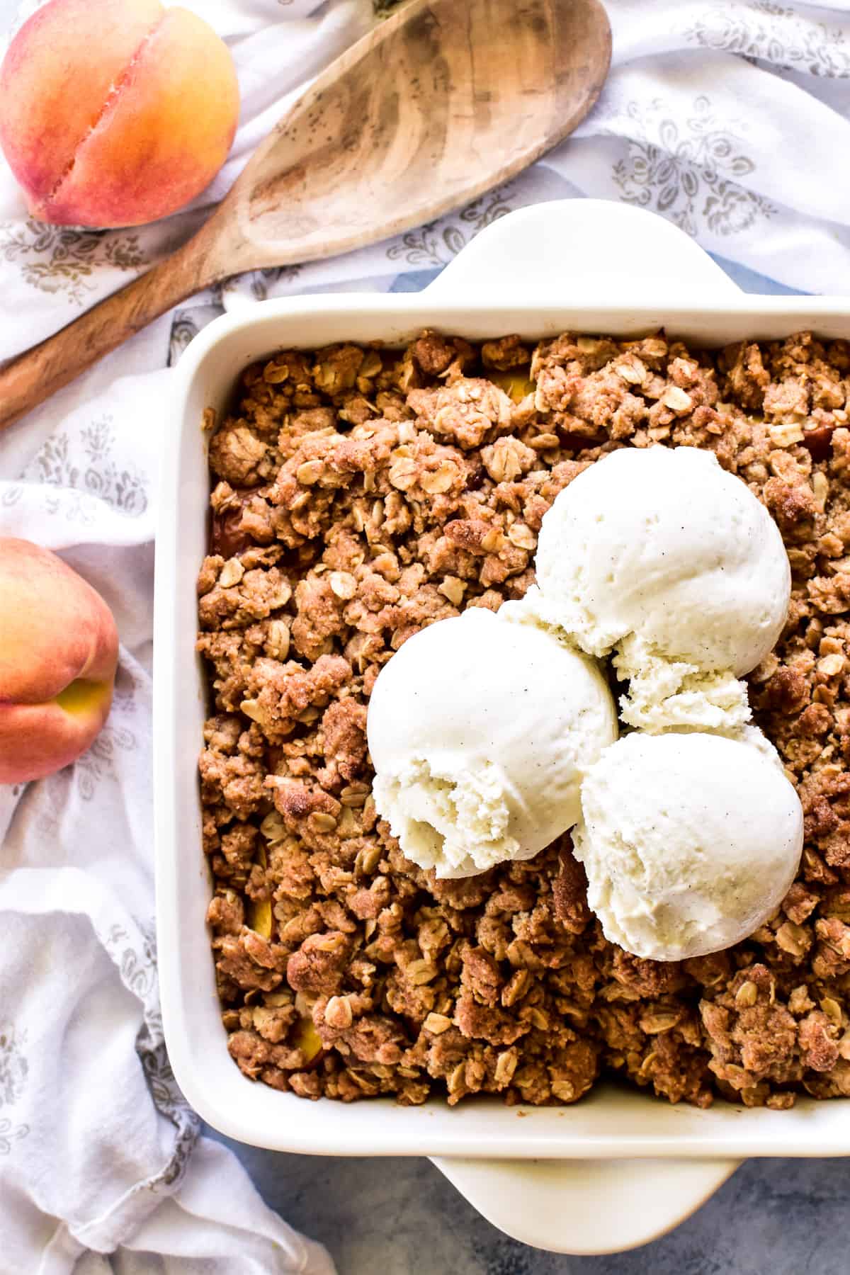 Overhead shot of peach Crisp in a baking pan with 3 scoops of vanilla ice cream